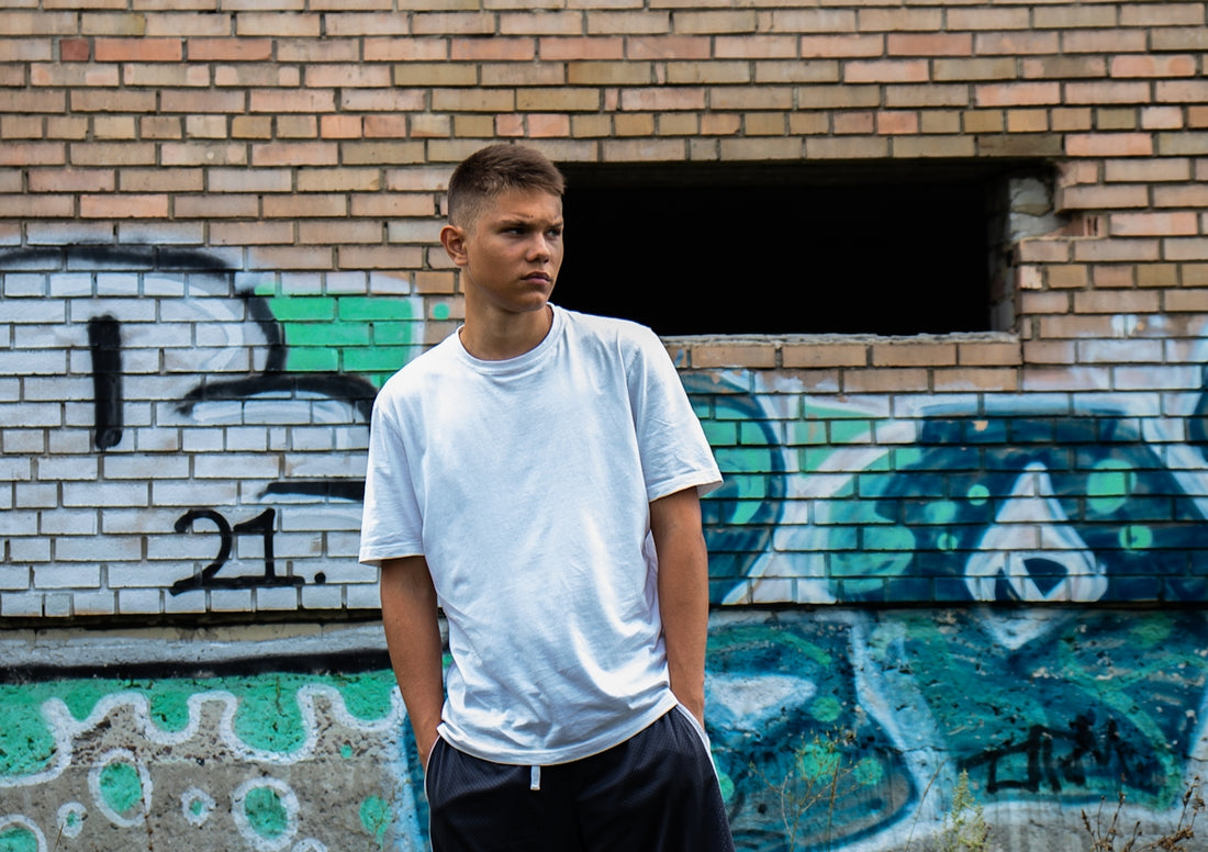 man in white crew neck t-shirt and black shorts standing near brown brick wall during